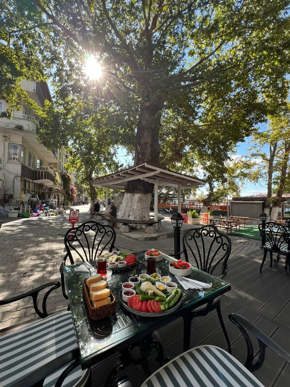 An outdoor dining area with a table set for a meal, surrounded by trees and a building in the background.