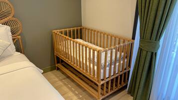 Une pièce avec un berceau en bois, un lit avec une literie blanche, une chaise en osier et des rideaux verts.
