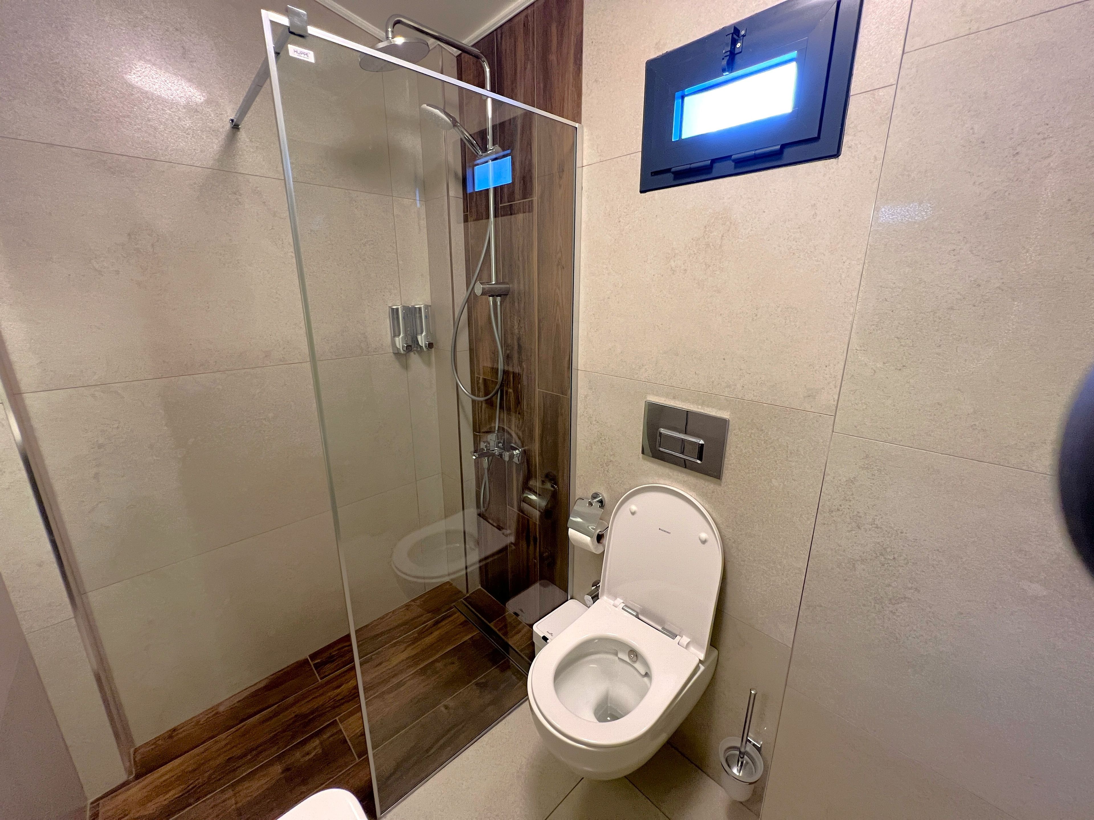 A modern bathroom with a glass-enclosed shower, a toilet, and a wall-mounted light fixture.