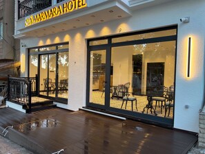 The exterior of Alamarra Hotel with large glass windows, a wooden deck, and a black railing. - Alâ Marmara Hotel (Marmara)