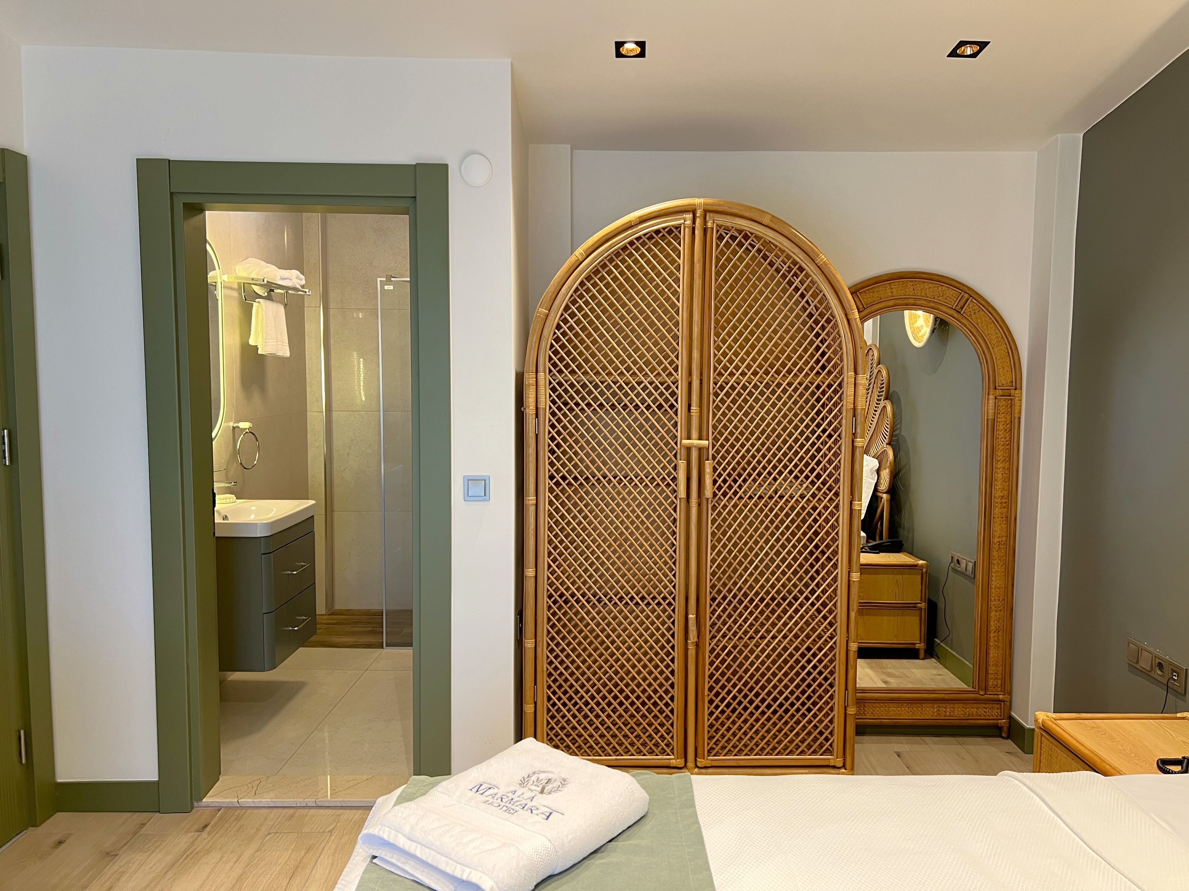 Ein Hotelzimmer mit einem Bett, einem Kleiderschrank mit Spiegel und einem durch eine offene Tür einsehbaren Badezimmer.