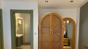 Habitación de hotel con cama, armario con espejo y baño visible a través de una puerta abierta.