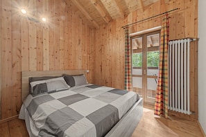 A wooden-paneled room with a bed, a window with curtains, and a radiator.