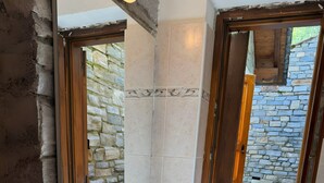 A bathroom with a large mirror, a sink, a toilet, and a window with a view of a stone wall.