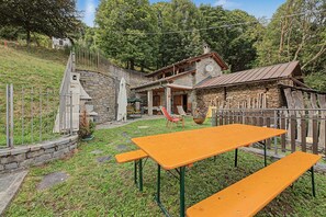 A rustic stone house with a wooden fence, a picnic table, and a small garden area.