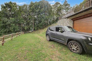 A vehicle parked on a grassy slope with a stone wall and wooden fence in the background.