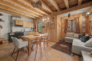 A cozy cabin interior with a wooden dining table, chairs, a sofa, and a kitchen area.