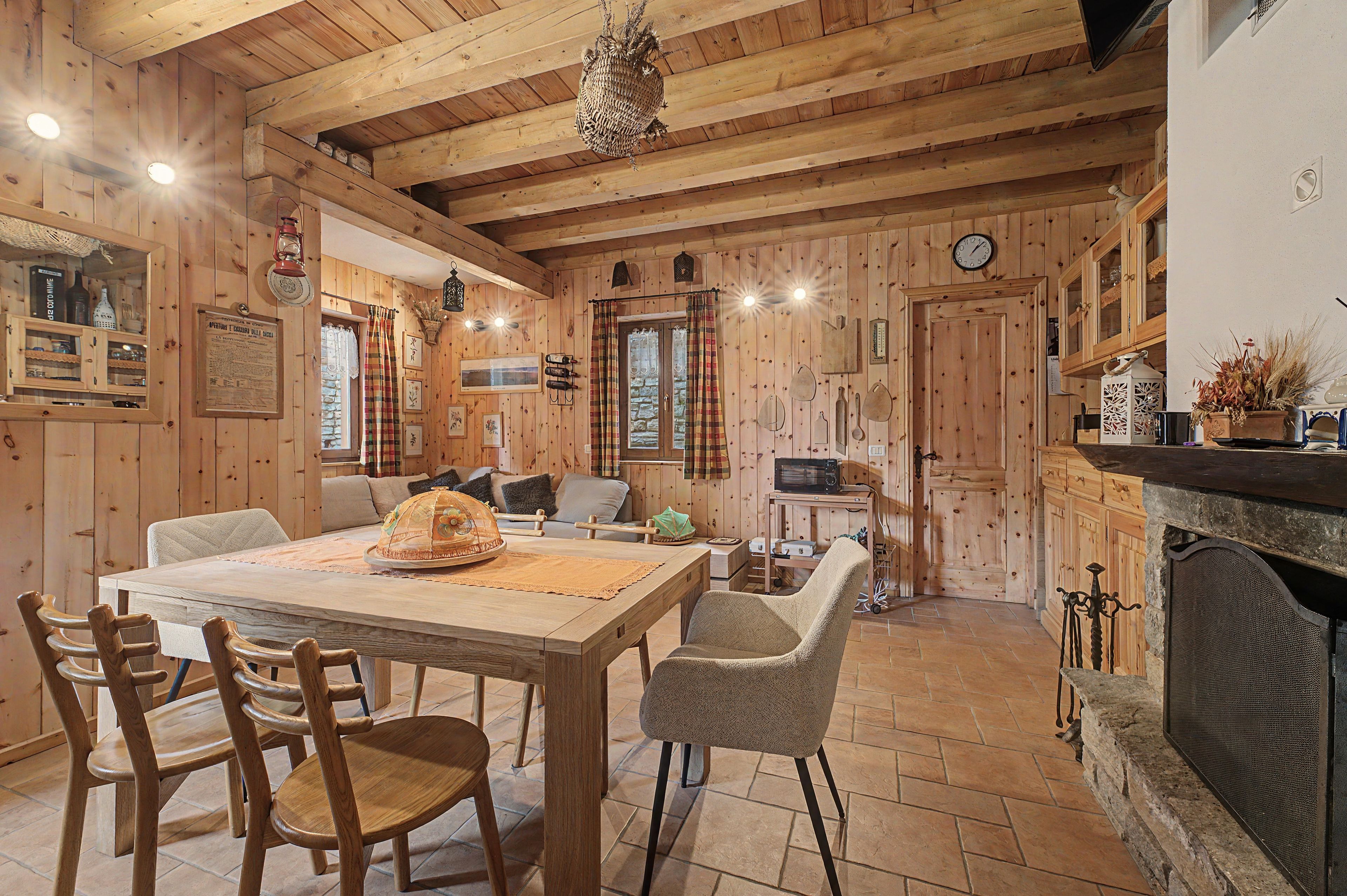 Ein Holzinterieur mit Esstisch, Stühlen, Kamin und Küchenzeile.