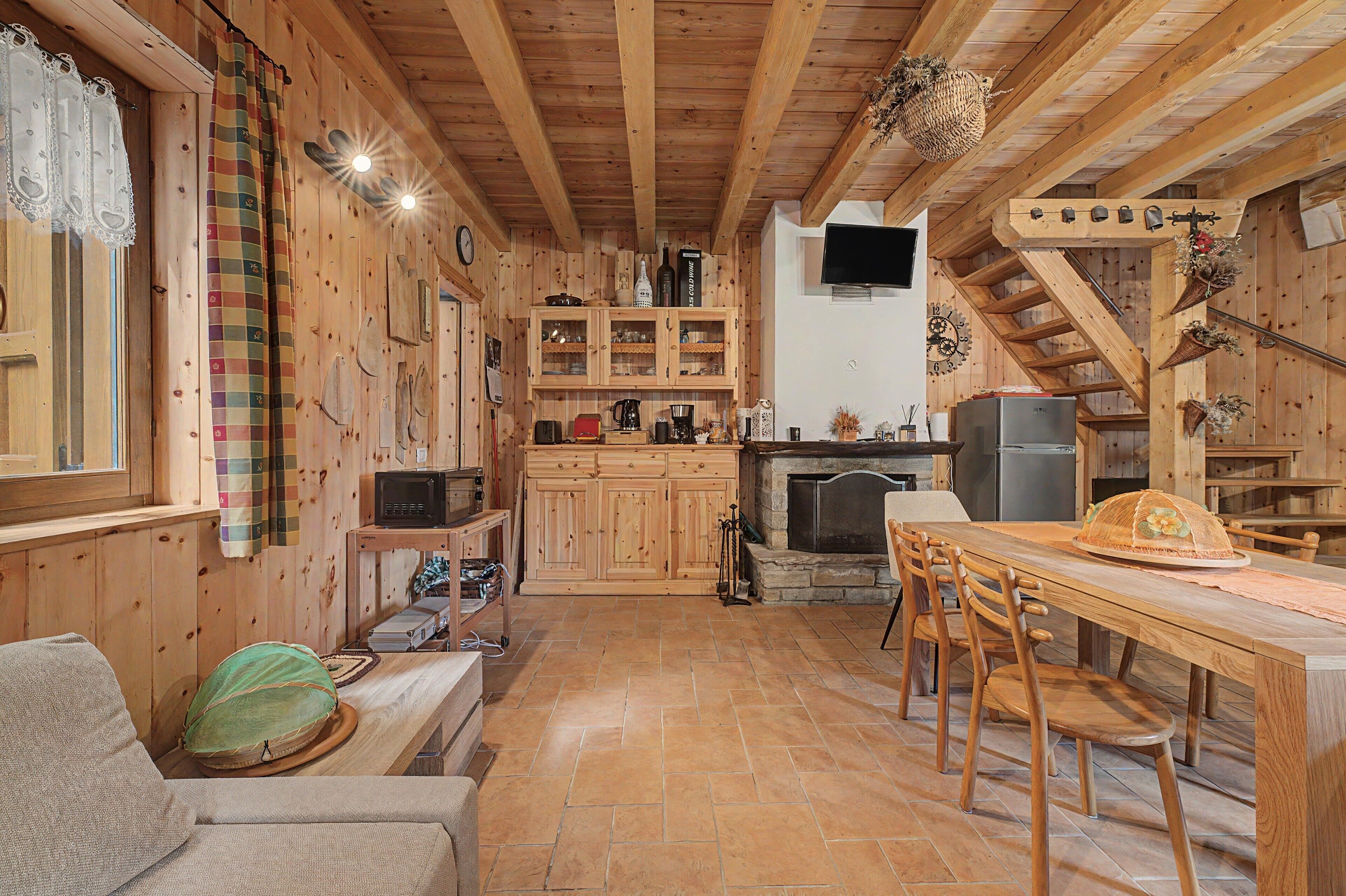 A cozy cabin interior with wooden walls, a stone fireplace, a dining area, and a kitchen with wooden cabinets and appliances.