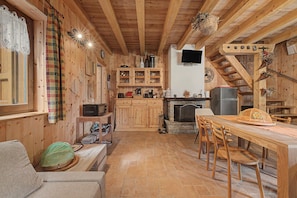 A cozy cabin interior with wooden walls, a stone fireplace, a dining area, and a kitchen with wooden cabinets and appliances.