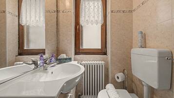 Et badeværelse med dobbeltvask, toilet, radiator og et vindue med gardin.