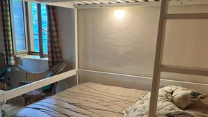 A bunk bed with a lower bunk, a window with curtains, a chair, and a small table.