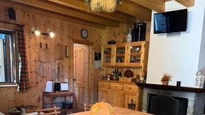 A wooden interior with a dining table, chairs, a fireplace, and a kitchen area.