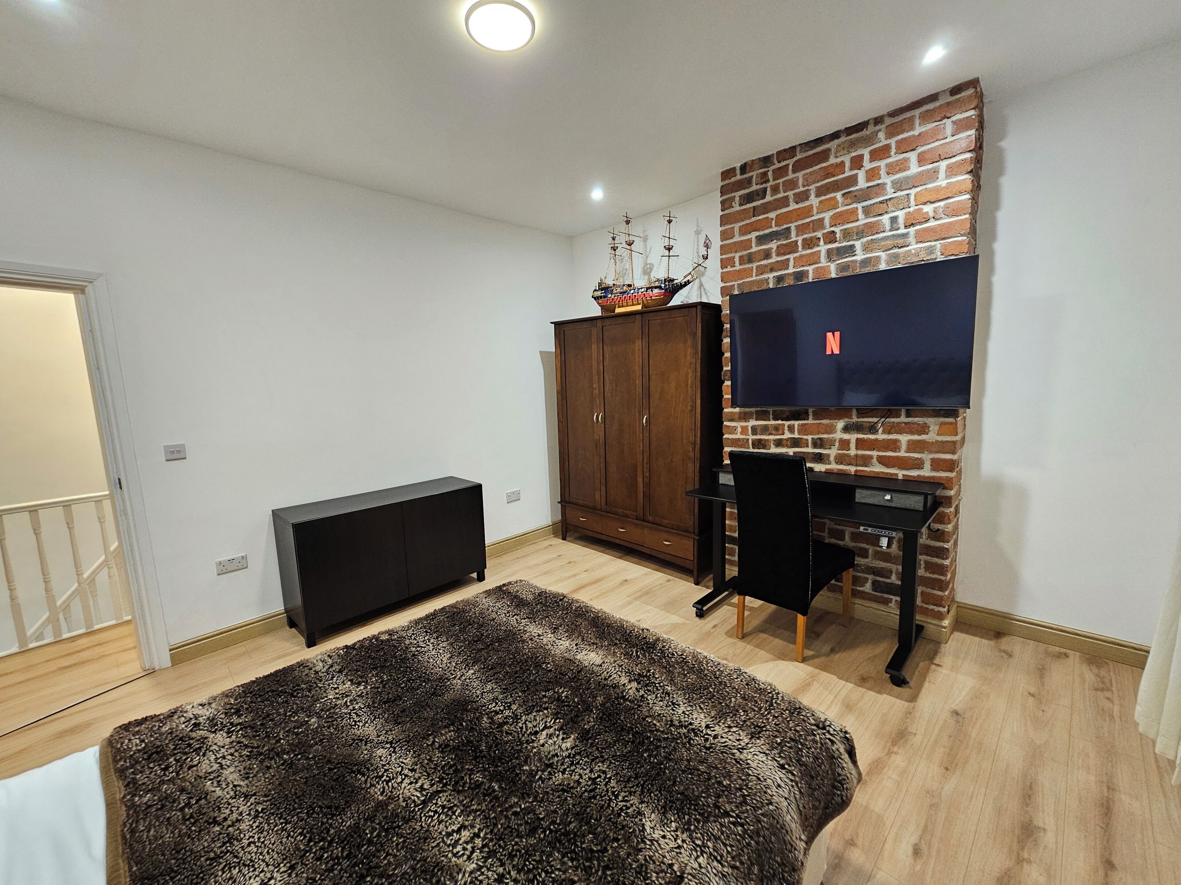 Ein Zimmer mit einem großen Flachbildfernseher an einer Ziegelwand, einem Holzschrank, einem schwarzen Schreibtisch und einem Leopardenfellteppich.