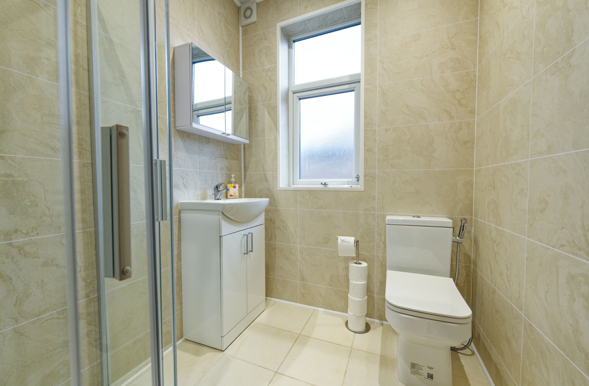 A bathroom with a toilet, sink, mirror, and a window.