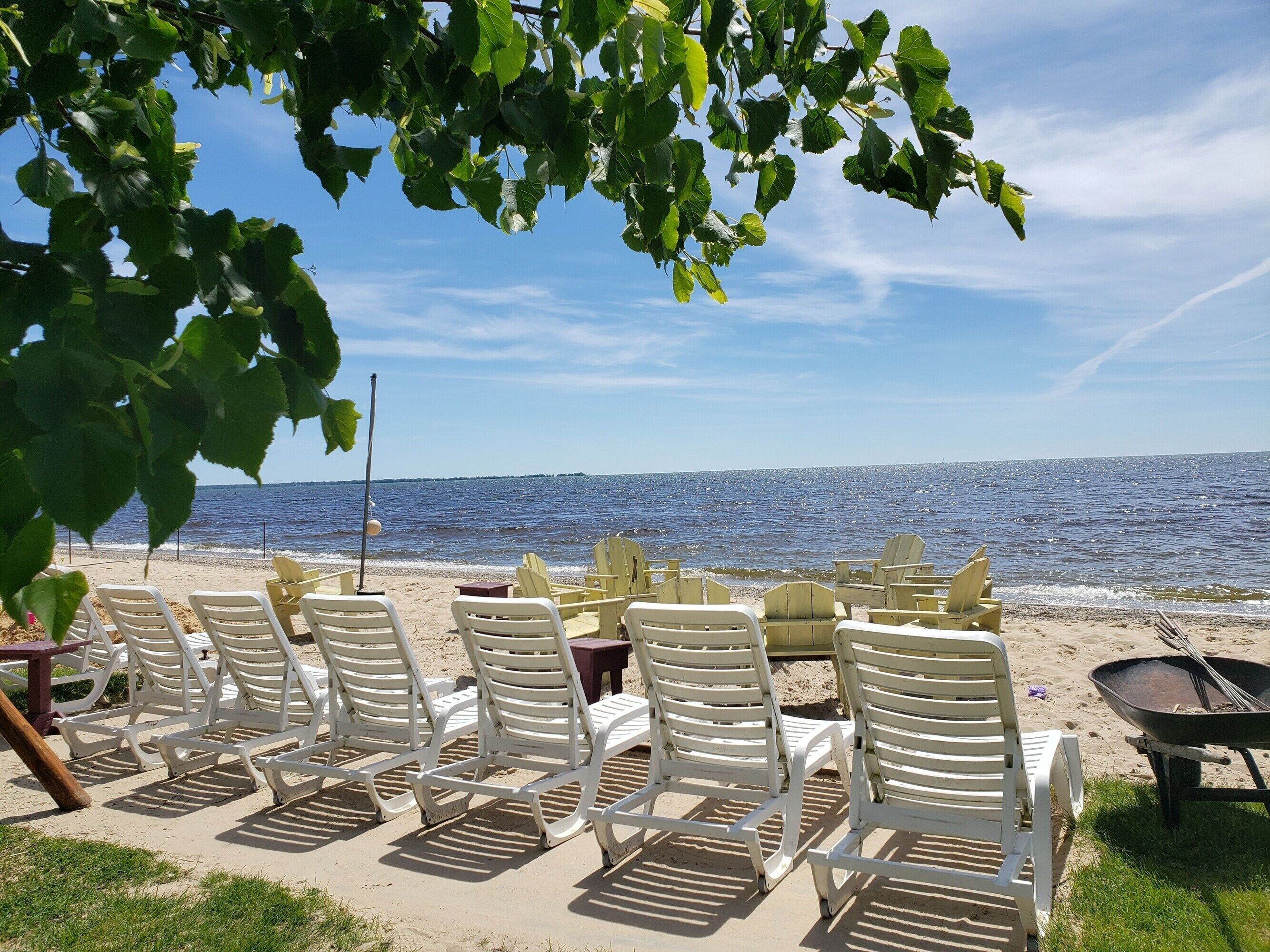 Un espace aménagé avec des sièges au bord de la plage, comprenant des chaises en plastique blanches et une brouette, offrant une vue sur une mer calme sous un ciel dégagé.