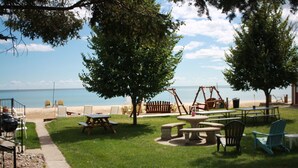 Et udendørs siddeområde med picnicborde og stole, en gynge samt udsigt til stranden.