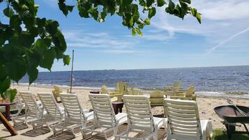 A beachside seating area with white plastic chairs and a wheelbarrow, overlooking a calm sea under a clear sky.