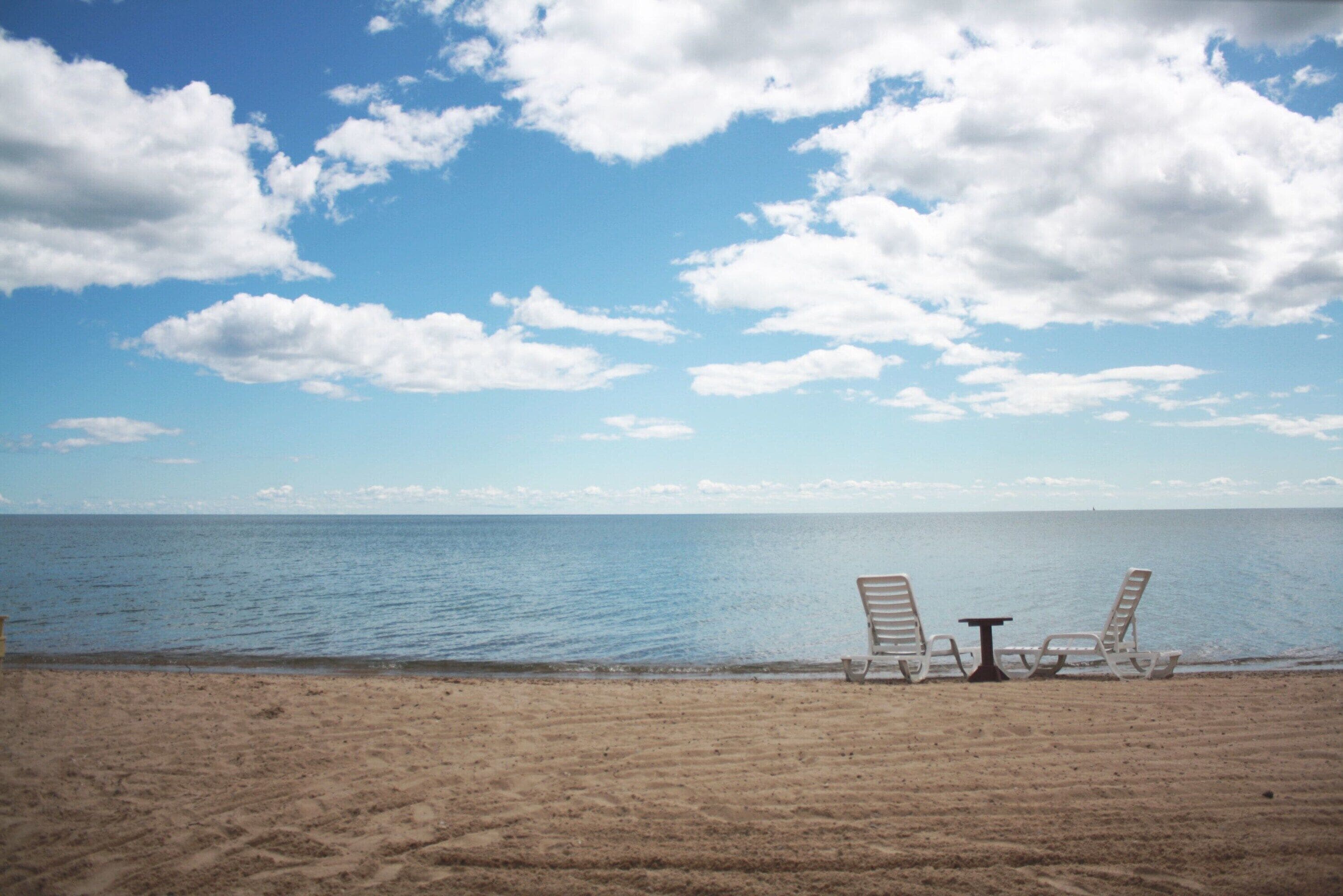 A beach with two lounge chairs and a small table facing the ocean.