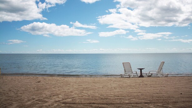 En strand med to liggestole og et lille bord med udsigt over havet.