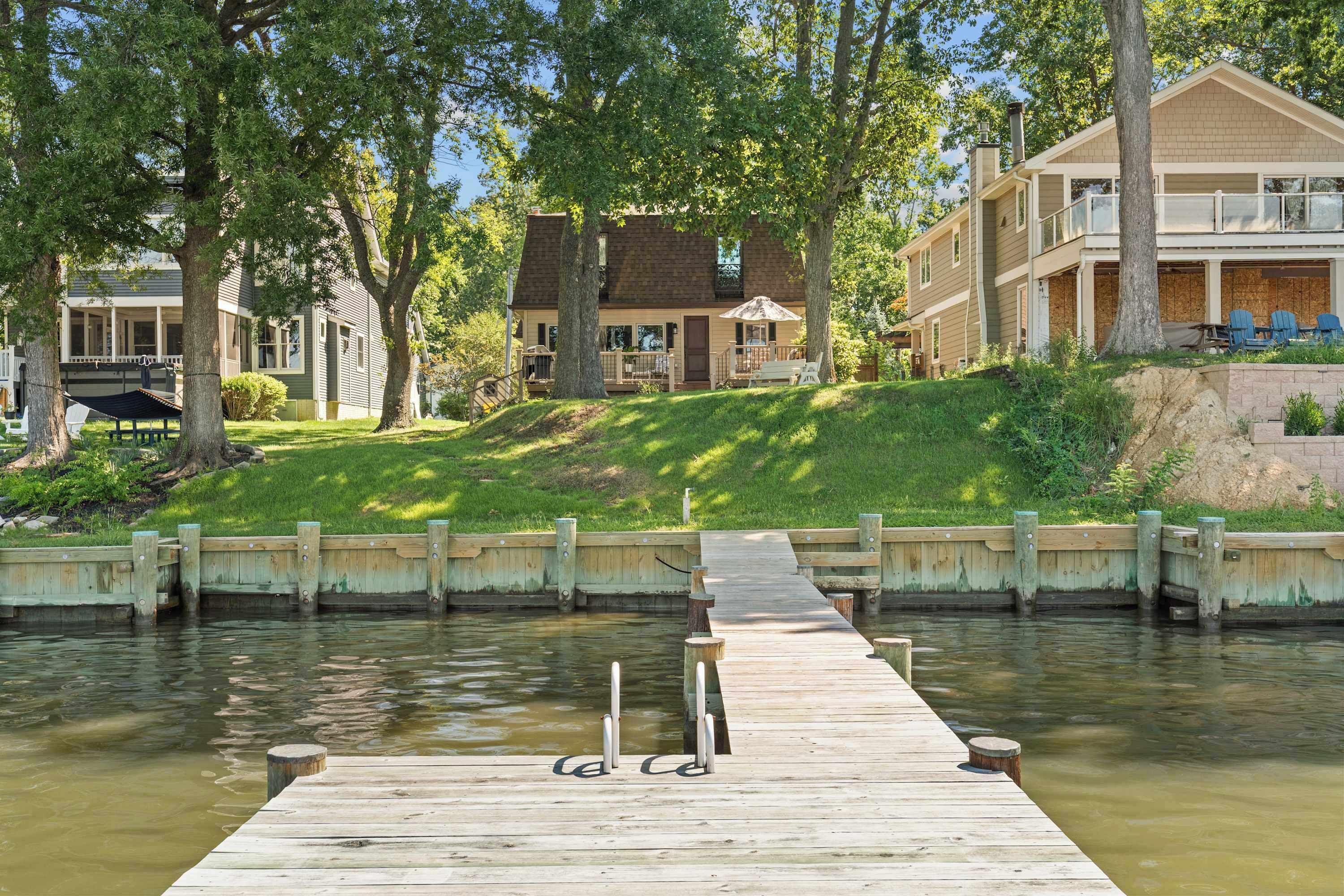 A wooden dock leading to a house with a porch and a covered outdoor seating area.