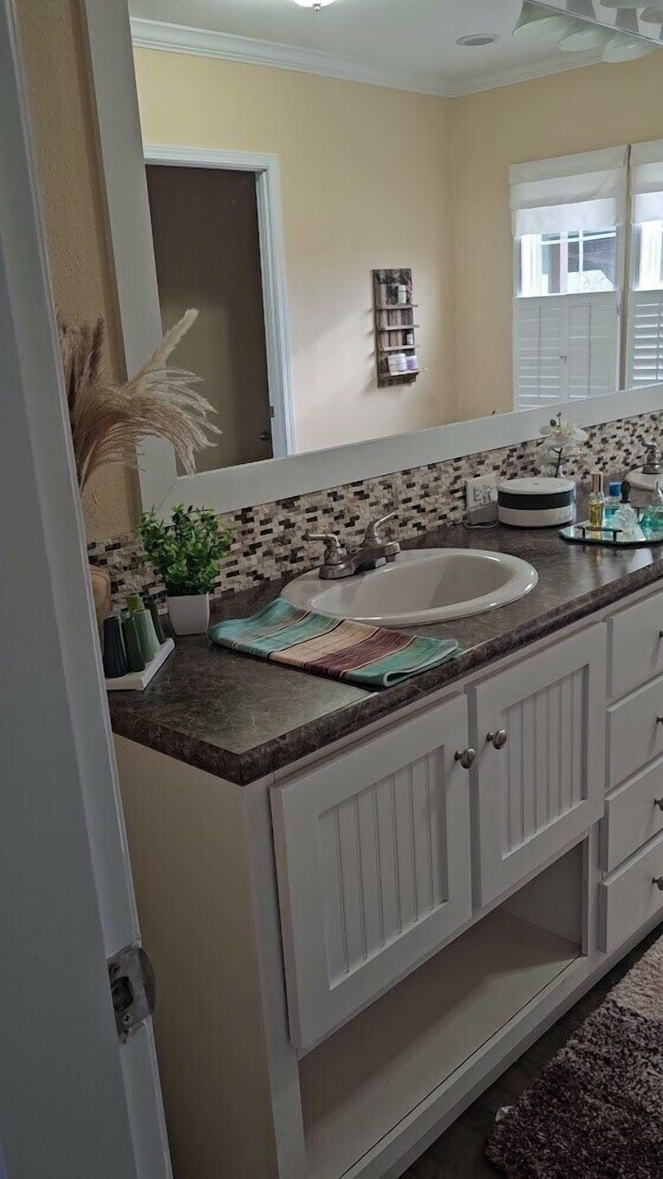 A bathroom with a white vanity, a sink, and a mirror. There is a decorative plant and a towel rack on the countertop.
