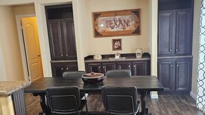 Un comedor con una mesa y sillas de madera oscura, una cocina con armarios oscuros y un letrero en la pared que dice 'TEXAN'.