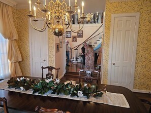 Ein Essbereich mit einem langen Tisch, der für eine Mahlzeit gedeckt ist, einer Chandelüster und einer Treppe im Hintergrund.