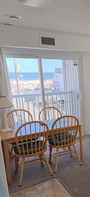 A room with a table and chairs, a window with a view of the beach, and a white door with a vent. - Ocean Views • 1-BR Ocean City NJ Condo • Beach Block • Boardwalk Ramp • King Bed (Ocean City)
