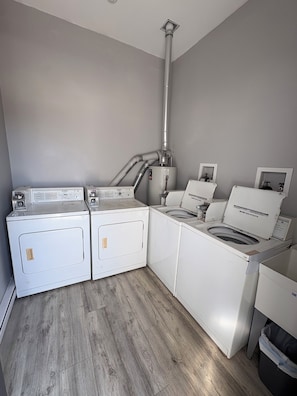 A laundry room with two front-loading washers and a dryer, a ventilation system, and a trash bin. - Ocean Views • 1-BR Ocean City NJ Condo • Beach Block • Boardwalk Ramp • King Bed (Ocean City)