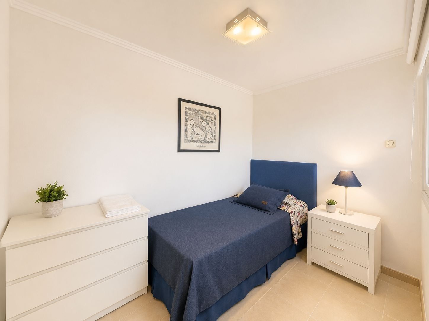 Ein Schlafzimmer mit Bett, Nachttisch, Lampe und einem gerahmten Bild an der Wand.