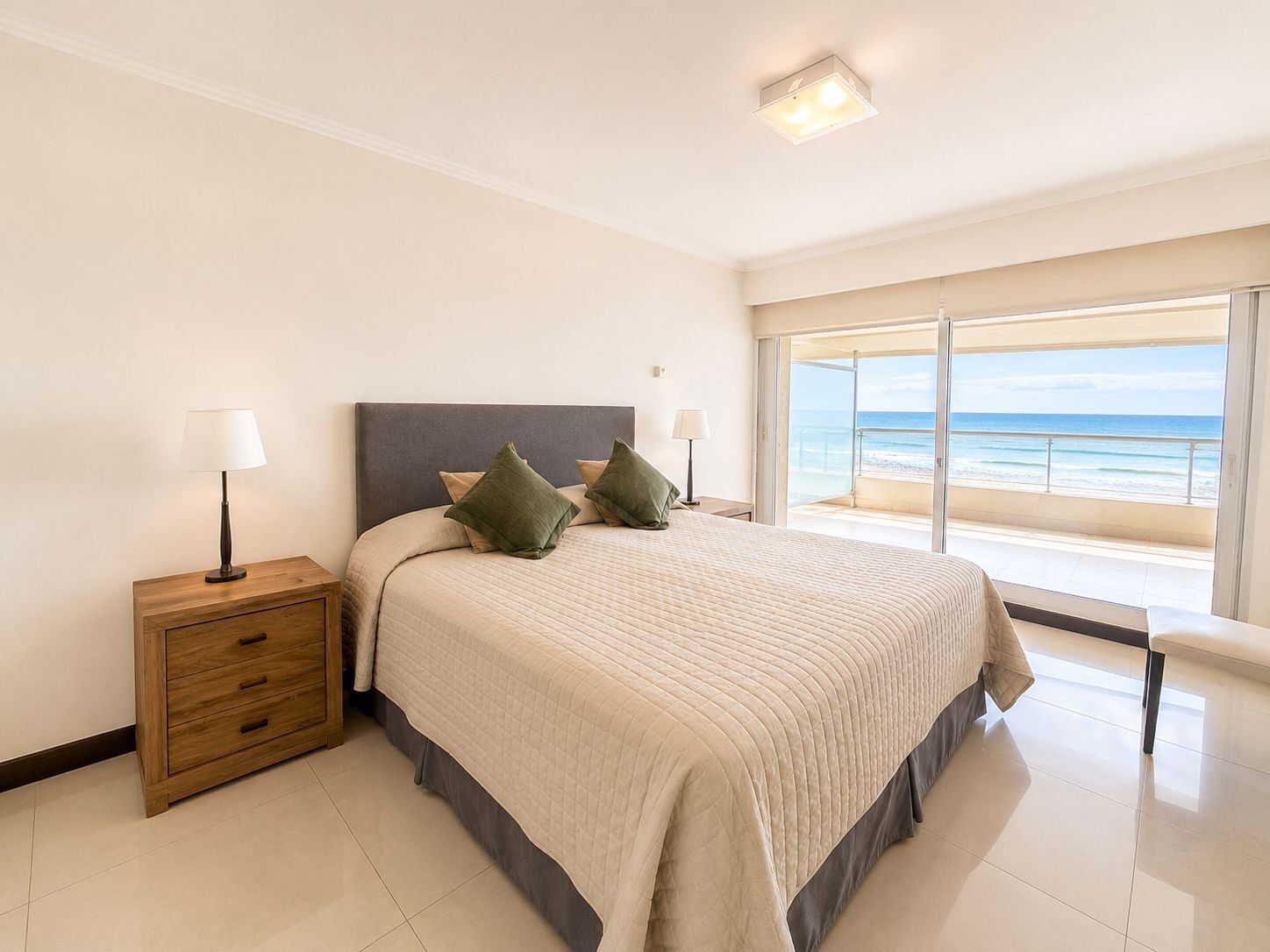 Une chambre à coucher avec un lit, des tables de chevet, une commode en bois et une vue sur l’océan.