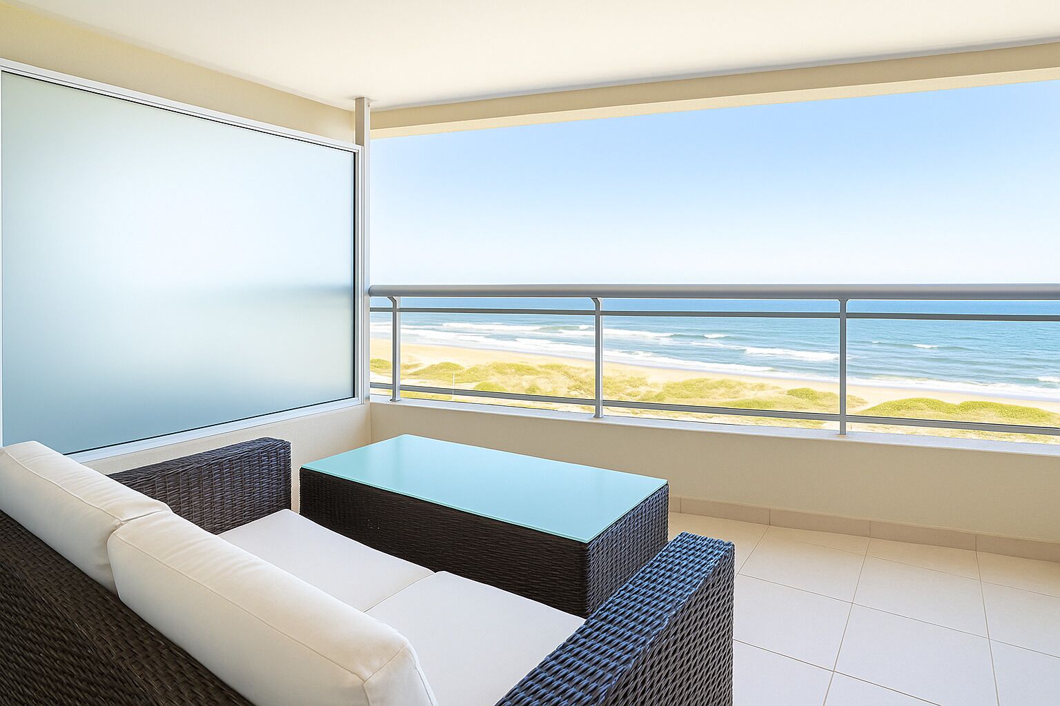 Un balcon avec vue sur la plage, un canapé blanc et une petite table.