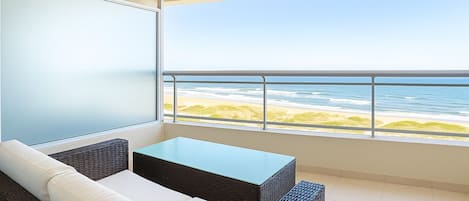 A balcony with a view of the beach, a white sofa, and a small table.
