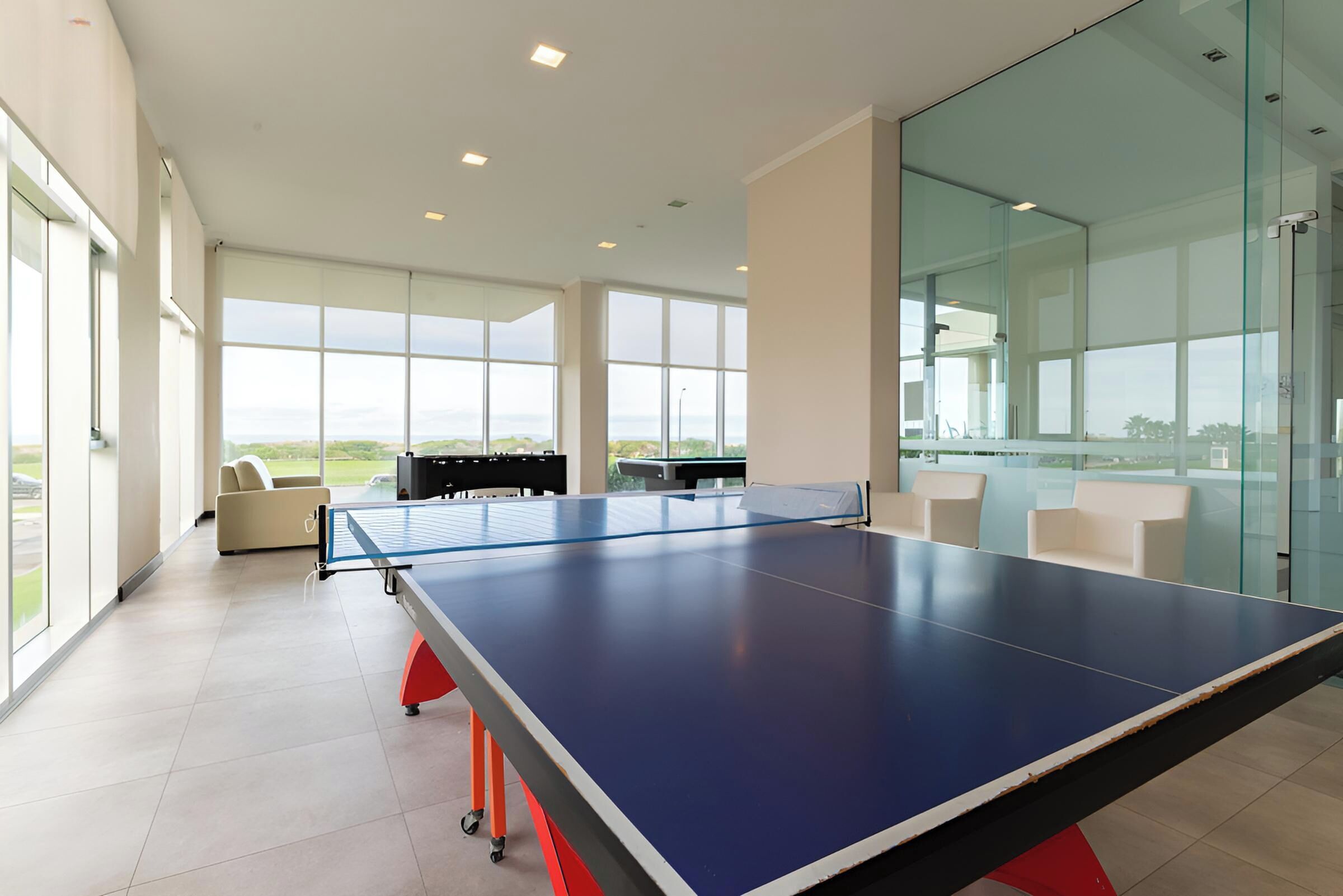 Una habitación amplia con mesa de ping pong, ventanas grandes y vistas al exterior.
