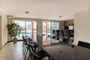 A spacious dining area with a long table and chairs, a potted plant, and a view of a swimming pool and buildings. - Luxury Apartment Across from the Best Beach (Punta Del Este)