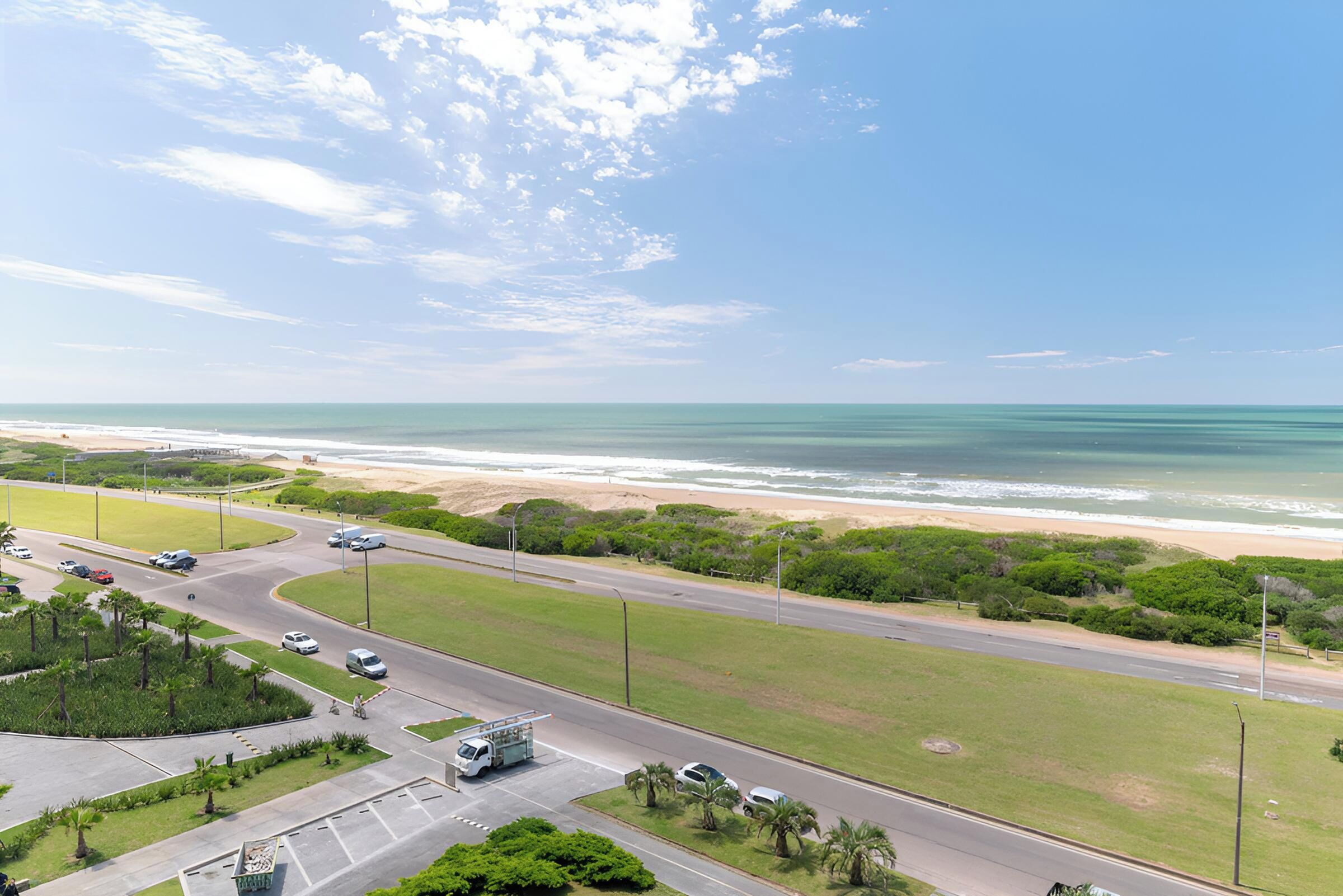 Una carretera costera con vista a la playa, vehículos y vegetación.