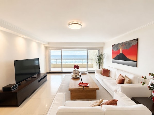 Una sala moderna con un televisor de pantalla plana, una mesa de centro de madera y un sofá blanco.