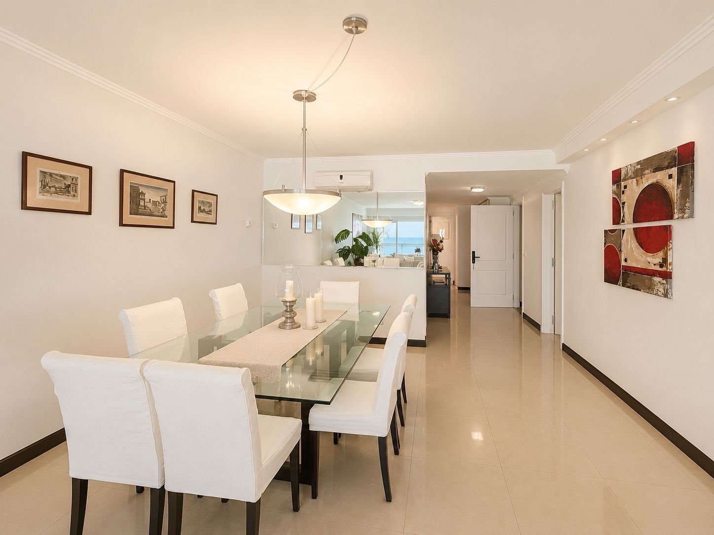 Un comedor moderno con una mesa de vidrio, sillas blancas y una lámpara colgante.
