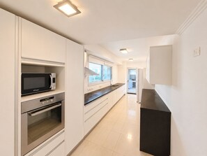 A modern kitchen with white cabinetry, a built-in microwave, an oven, and a black countertop. - Luxury Apartment Across from the Best Beach (Punta Del Este)