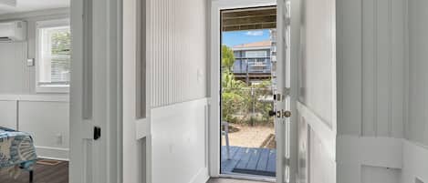 A narrow hallway leading to a door with a view of a balcony and outdoor area.
