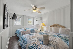 A hotel room with two beds, a ceiling fan, a TV mounted on the wall, and a window with blinds. - Cherry Grove 4BR Ground Floor · Pet-Friendly (North Myrtle Beach)