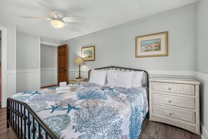 Ein Schlafzimmer mit einem Bett, einem Nachttisch, einer Kommode, einem Deckenventilator und zwei gerahmten Bildern an der Wand.