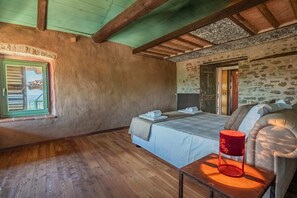 Ein Schlafzimmer mit Holzboden, einem Bett mit weißen Leinen, einer roten Lampe und einem Fenster mit Fensterläden.