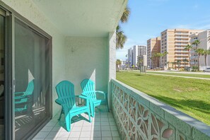 A balcony with turquoise chairs, a view of a grassy area, and tall buildings in the background. - 🏁 Ocean Terrace Club 107 | Ground Floor | Steps to Daytona Beach (Daytona Beach Shores)