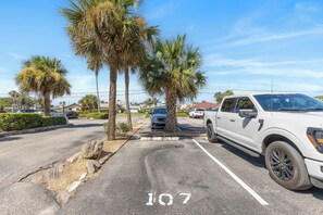 A parking lot with palm trees, a white pickup truck, and a building in the background. - 🏁 Ocean Terrace Club 107 | Ground Floor | Steps to Daytona Beach (Daytona Beach Shores)