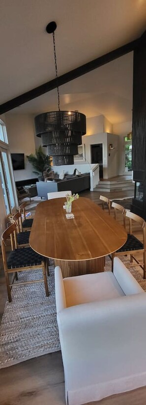 Un comedor moderno con una gran mesa de madera, sillas blancas tapizadas y una lámpara colgante negra.