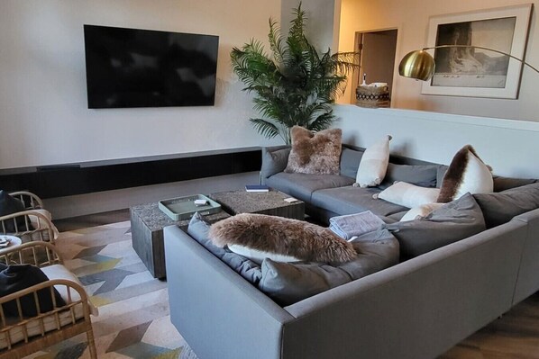 Una sala de estar moderna con un sofá gris, una mesa de centro y un televisor de pantalla plana montado en la pared.