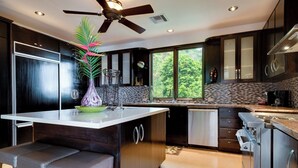 A modern kitchen with a central island, dark cabinetry, and a view of greenery outside. - Vivara: Private House, PH & 5 Villas 180° Ocean View, Dominical CR-16 guest (Savegre de Aguirre, Puntarenas Province)