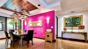 A dining area with a wooden ceiling, a pink accent wall, and a painting of a jungle scene. - Vivara: Private House, PH & 5 Villas 180° Ocean View, Dominical CR-16 guest (Savegre de Aguirre, Puntarenas Province)